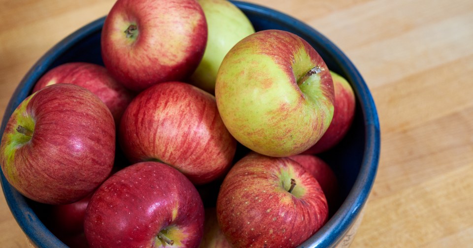 A blue bowl filled with fresh red apples on a wooden surface