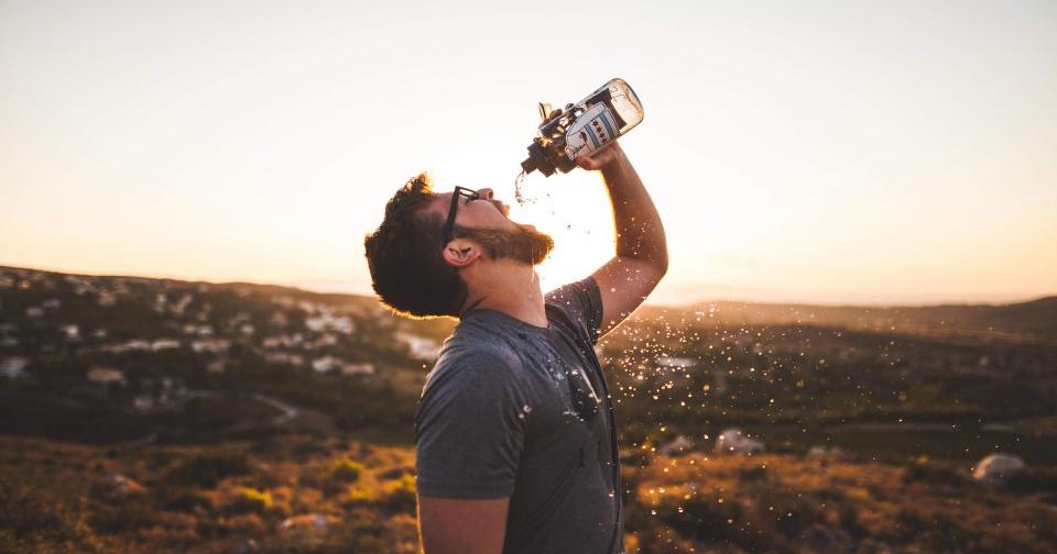 A man drinking water from a bottle outdoors at sunset