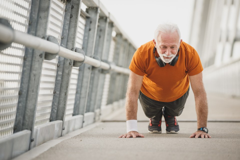 An older man doing a push-up outdoors on a bridge